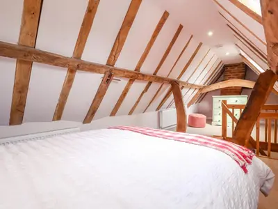 a white bed in a room with wooden beams at Brook Cottage in Saxmundham