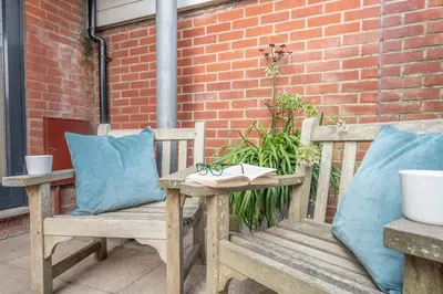 two wooden benches with pillows and a table with a book at Captain's Quarters, a ground floor apartment in Aldeburgh in Aldeburgh