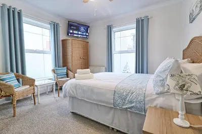 a bedroom with a bed and two chairs and windows at Walton Beach Holiday Lets in Walton-on-the-Naze
