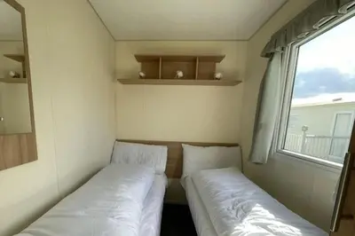 two beds in a small room with a window at 3 Bed Caravan Sleeps 8 - Parking Bbq Pool in Clacton-on-Sea