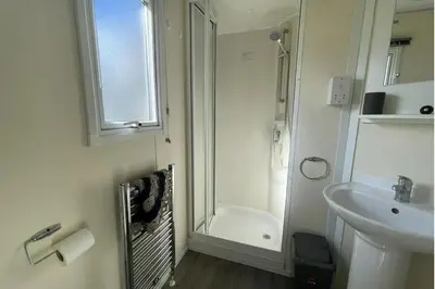 a white bathroom with a shower and a sink at 3 Bed Caravan Sleeps 8 - Parking Bbq Pool in Clacton-on-Sea