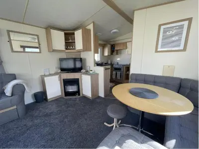 a small living room with a table and a kitchen at 3 Bed Caravan Sleeps 8 - Parking Bbq Pool in Clacton-on-Sea