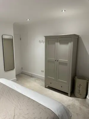 a white room with a cabinet and a mirror at The Snug - Town Centre Apartment in Bishops Stortford