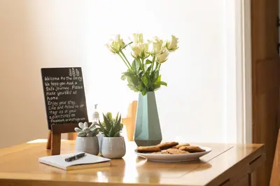 a table with a vase with flowers and a plate of cookies at Harestreet Farm Barns, The Dairy, Parlour and Creamery in Cottered
