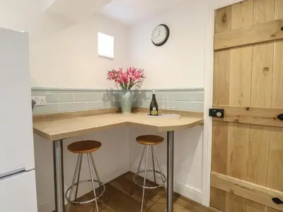 a kitchen with two bar stools and a clock on the wall at Pear Tree Cottage in Swaffham