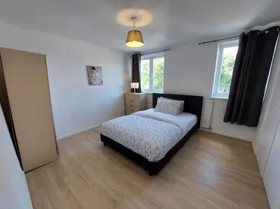 a bedroom with a bed and two windows at 5 Bedroom House in Romford in Harold Wood