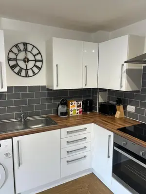 a kitchen with white cabinets and a clock on the wall at The Nook - Town Centre Apartment in Hoddesdon