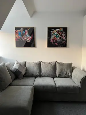 a couch in a living room with three paintings on the wall at The Nook - Town Centre Apartment in Hoddesdon