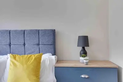 a bed with a blue headboard and a lamp on a table at Elm Cottage Ipswich in Ipswich