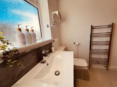 a bathroom with a sink and a window with bottles on it at The Palm Tree House in St Ives