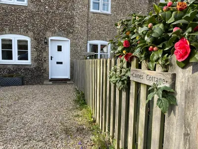 a house with a fence with a flower bush on it at Caines Cottage in Saxmundham