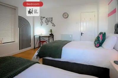 a bedroom with two beds and a clock on the wall at Quiet Premium Stansted Apartment in Central Location with WiFi and Desk in Stansted Mountfitchet