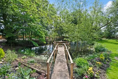 a wooden bridge in a garden with flowers at Stunning 2 Lodge Cottage retreat in Little Saxham