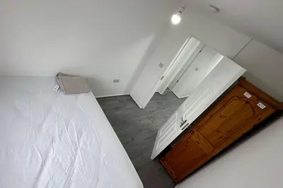 a white bedroom with a bed and a wooden cabinet at Diamond House in Friern Barnet