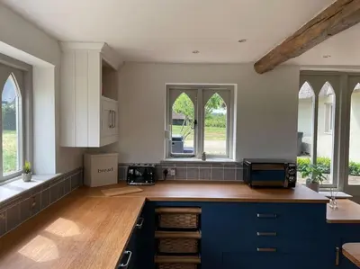 a large kitchen with blue cabinets and windows at Old Cottage - English Countryside Retreat in Lindsell