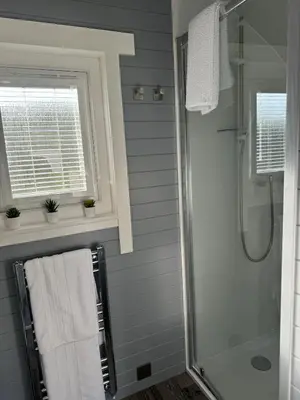 a bathroom with a shower and a window and towels at Windmill Glamping Pod with hot tub - The Snug in Swavesey