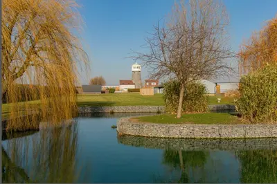 a pond in front of a farm with a water tower at Windmill Glamping Pod with hot tub - The Snug in Swavesey