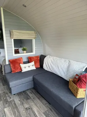 a blue couch with colorful pillows on a porch at Windmill Glamping Pod with hot tub - The Snug in Swavesey