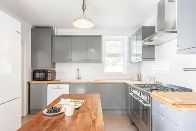 a white kitchen with a wooden table in it at The Red House, Leiston in Woodbridge