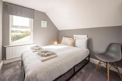 a bedroom with a white bed with a chair and a window at The Red House, Leiston in Woodbridge