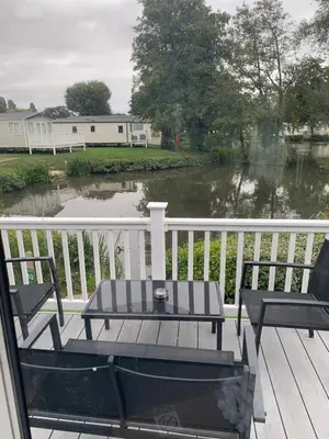 a table and chairs on a deck with a view of a river at Lakeside Lodge Valencia 2 bedroom in Weeley