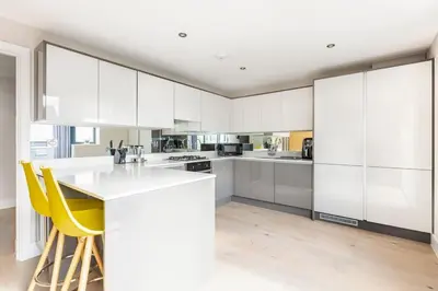 a white kitchen with white cabinets and yellow chairs at Contemporary 3 Bedroom Fully Detached Town House in Wickford