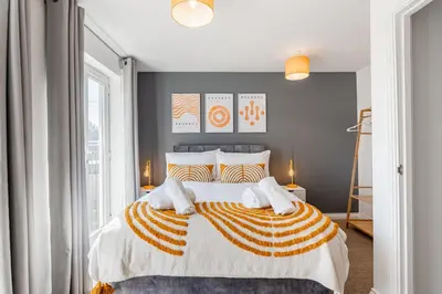 a bedroom with a large bed with orange and white pillows at Caboose Stays - Bury St Edmunds - Modern 4 Bed townhouse close to centre and major transport links - Fast Wifi - Parking - Business and Contractors in Bury Saint Edmunds