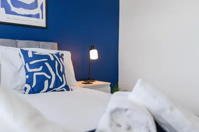 a bedroom with a bed with blue walls and a lamp at Caboose Stays - Bury St Edmunds - Modern 4 Bed townhouse close to centre and major transport links - Fast Wifi - Parking - Business and Contractors in Bury Saint Edmunds