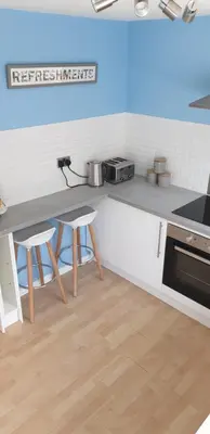 a kitchen with a counter with a table and stools at Rainbow on Sea Frinton-on-Sea in Kirby Cross