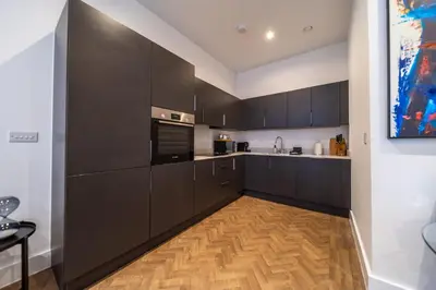 a kitchen with black cabinets and a wooden floor at The Essex Apartments - Ashby House in Chelmsford