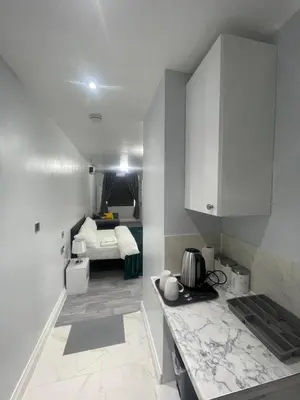 a kitchen with white cabinets and a bed in the background at Premium studio flat rental in Havering atte Bower