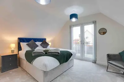 a bedroom with a bed and a window and a chair at Kestrel Gardens Five Bedroom Homes in Great Dunmow