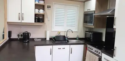 a kitchen with white cabinets and a sink and a microwave at Amazing Lodge with Hot Tub in Stowmarket