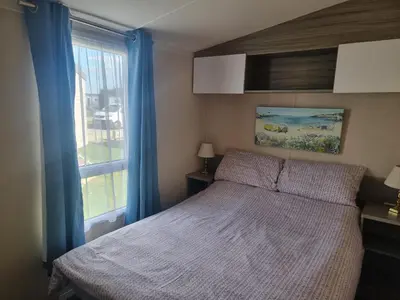 a bedroom with a bed with blue curtains and a window at HAPs Holiday Home - Haven The Orchards in Brightlingsea