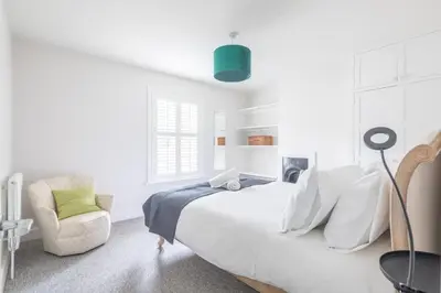 a white bedroom with a large bed and a chair at Beautiful 2Bed cottage nr City in Cambridge