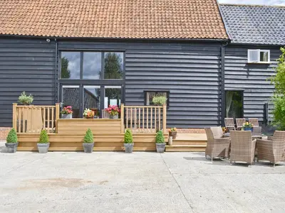 a house with a deck with chairs and potted plants at Rose Farm Barn in Laxfield