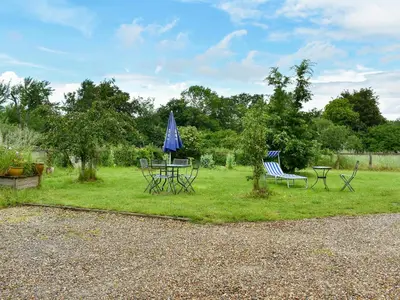 two chairs and a table with a blue umbrella at Evie Rose Cottage in Elsenham