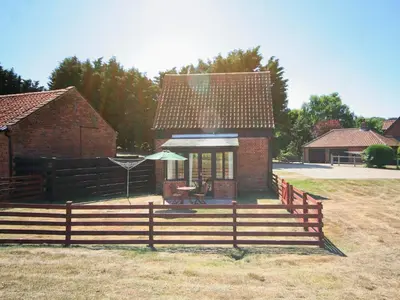 a small brick house with a fence and an umbrella at Sally's Nest - E3042 in Blyford