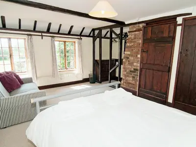 a bedroom with a white bed and a chair and window at Field Cottage in Sudbourne