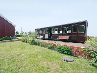 a train parked next to a garden with a bench at Railway Carriage One - E5337 in Wetheringsett