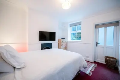 a white bedroom with a bed and a tv at Lower Cedars, Saxmundham in Saxmundham
