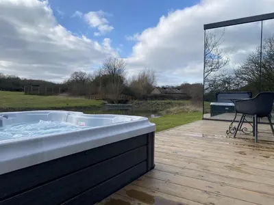 a jacuzzi tub on a wooden deck with a chair at Mirror Houses Pound Farm - Pond OOD in Saxmundham