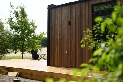 a wooden cabin with a chair on a wooden deck at Mirror Houses Pound Farm - Pond OOD in Saxmundham