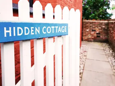 a white picket fence with a blue sign on it at Hidden Cottage by The Suffolk Cottage Collection in Aldeburgh