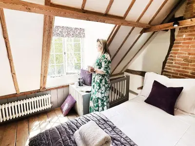 a woman standing in a room with a bed at The Cottage by The Suffolk Cottage Collection in Peasenhall