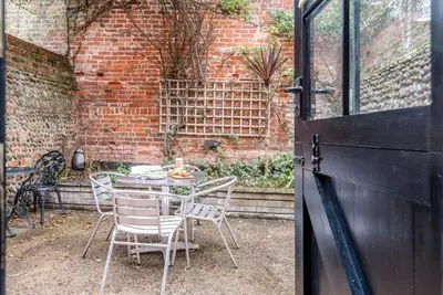 a table and chairs in a courtyard with a brick wall at Ann Page Cottage, Aldeburgh in Aldeburgh