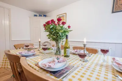 a dining room table with a vase of red roses at Ann Page Cottage, Aldeburgh in Aldeburgh