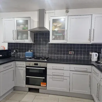 a kitchen with white cabinets and a stove top oven at Cosy large double room in Basildon