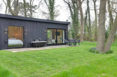 a black house with a bed and a tub in a yard at The Woods - Luxury cabin in a woodland setting in Hatfield Broad Oak