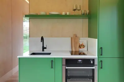 a kitchen with green cabinets and a sink and a stove at The Woods - Luxury cabin in a woodland setting in Hatfield Broad Oak